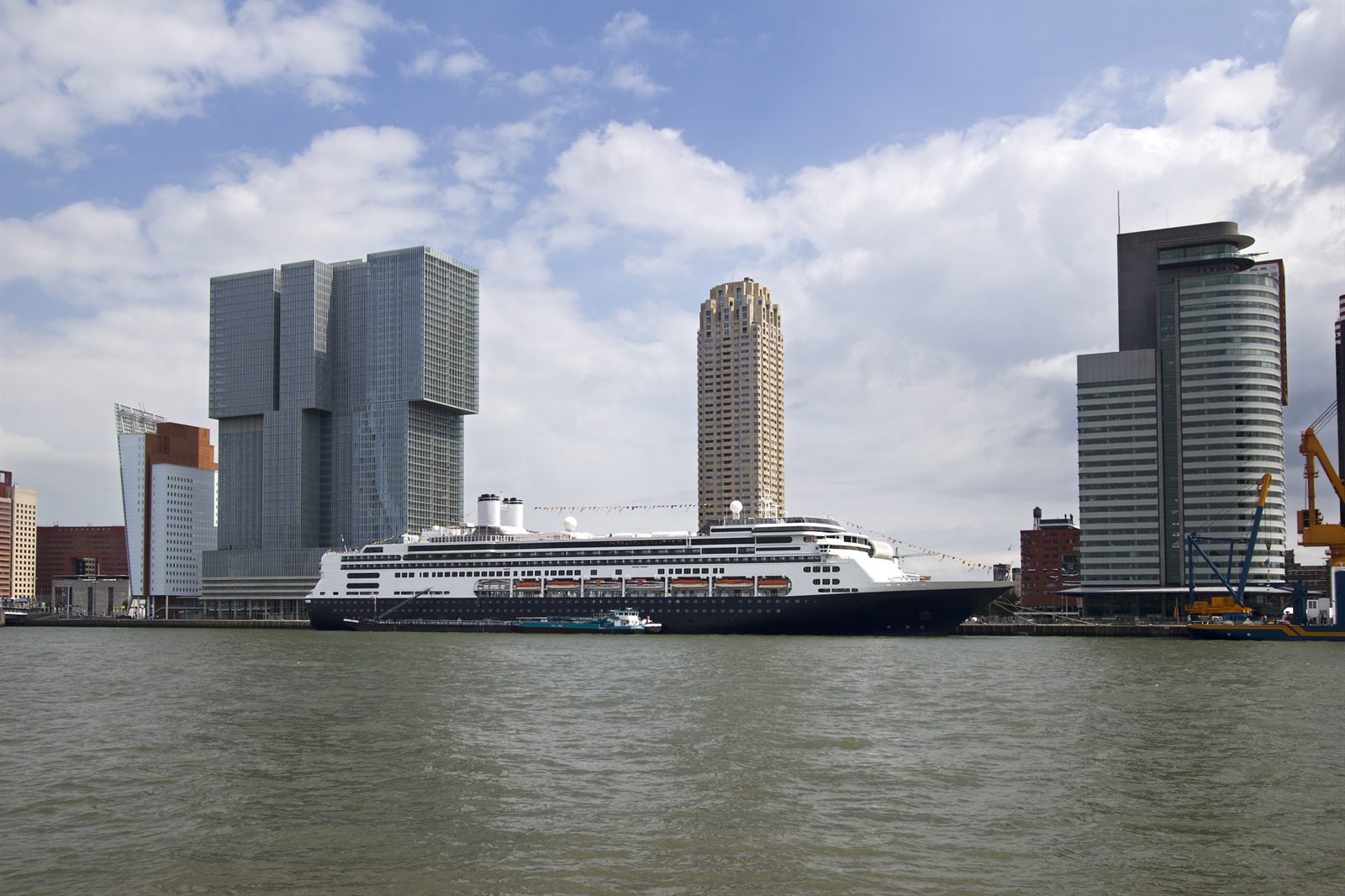 Cruise ship docked beside modern towers on a harbor waterfront, the kind of sailing people book online