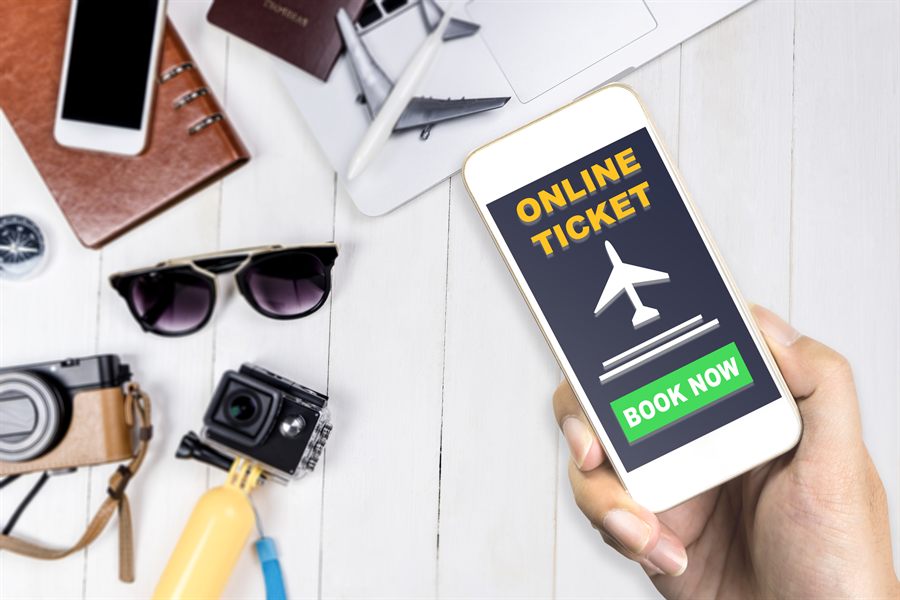Hand holding a phone with an online ticket and book now button, next to sunglasses and cameras