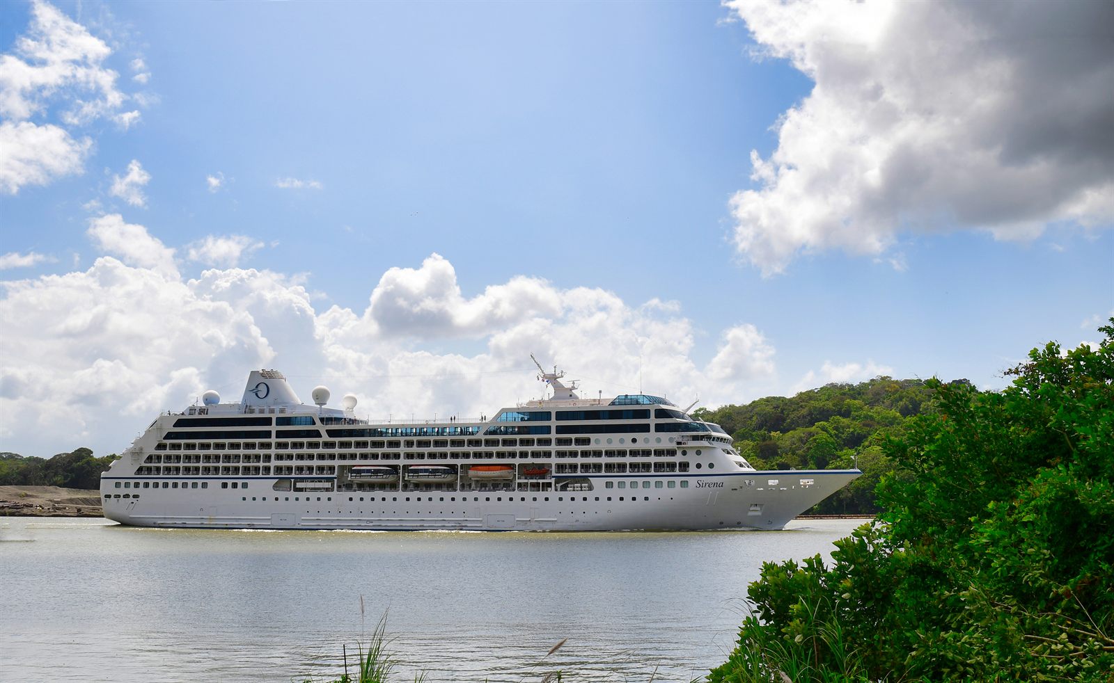 White cruise ship sailing past a green shoreline under a blue sky